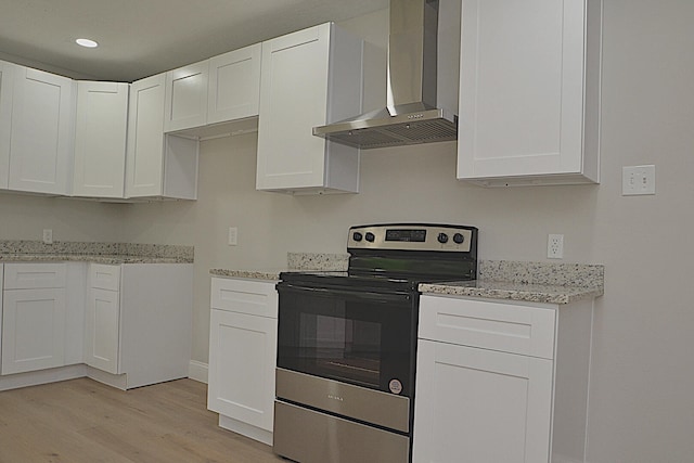 kitchen featuring stainless steel electric range, white cabinets, light stone countertops, light hardwood / wood-style flooring, and wall chimney range hood