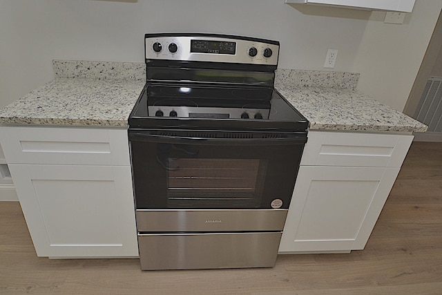 kitchen with stainless steel range with electric stovetop, light hardwood / wood-style flooring, light stone counters, and white cabinets