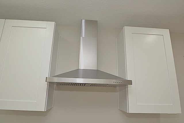 details with a textured ceiling and wall chimney range hood