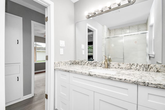 bathroom with ceiling fan, hardwood / wood-style floors, a shower with shower door, and vanity