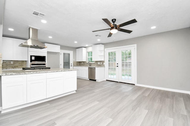 kitchen featuring white cabinets, wall chimney exhaust hood, light stone countertops, french doors, and stainless steel dishwasher