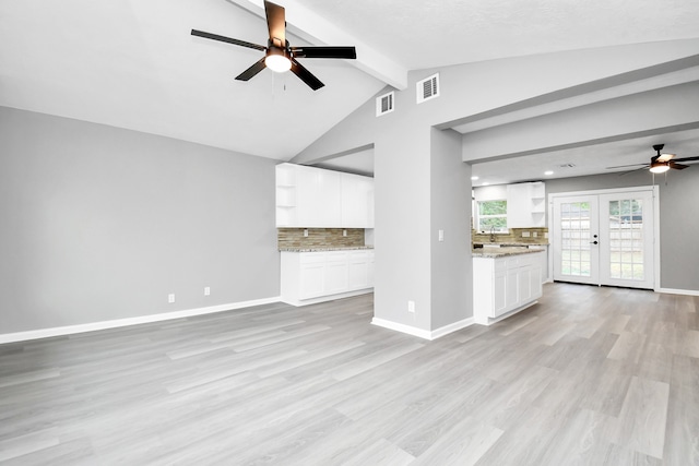 unfurnished living room featuring a textured ceiling, ceiling fan, light hardwood / wood-style flooring, french doors, and vaulted ceiling with beams