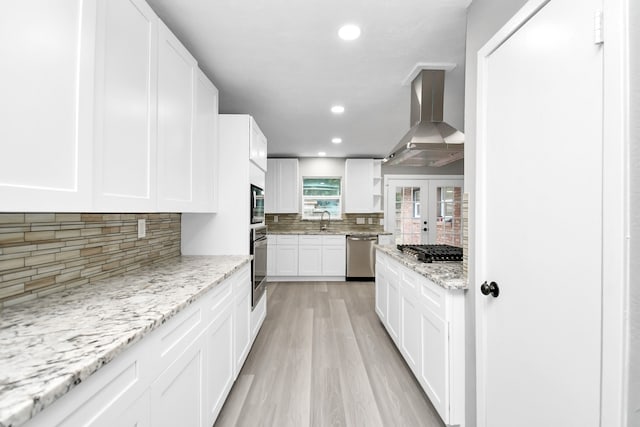 kitchen featuring white cabinetry, backsplash, wall chimney exhaust hood, stainless steel appliances, and light hardwood / wood-style flooring