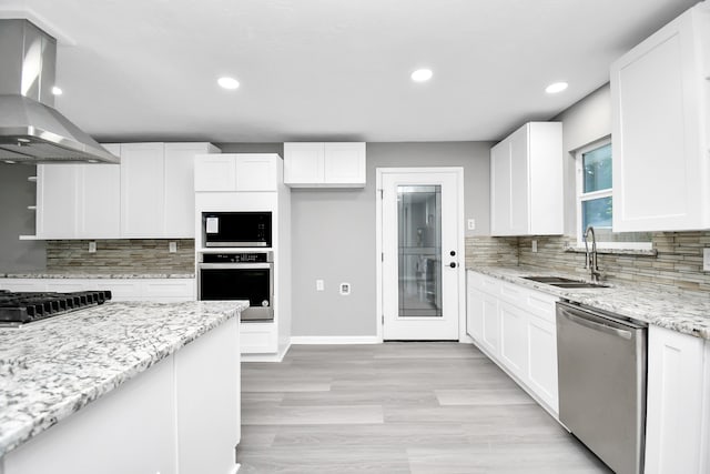 kitchen featuring sink, wall chimney exhaust hood, white cabinetry, stainless steel appliances, and light stone countertops