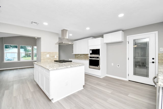 kitchen featuring light stone counters, tasteful backsplash, white cabinetry, wall chimney range hood, and appliances with stainless steel finishes