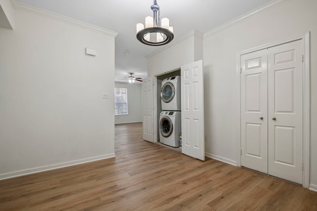 laundry area with ceiling fan with notable chandelier, stacked washer and clothes dryer, light wood-type flooring, and ornamental molding