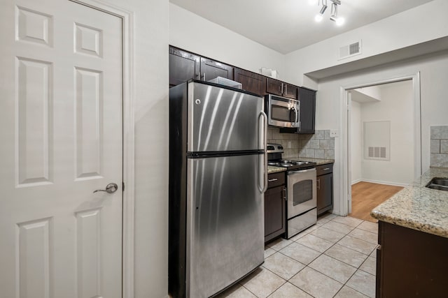 kitchen with tasteful backsplash, stainless steel appliances, light tile patterned floors, dark brown cabinetry, and light stone countertops