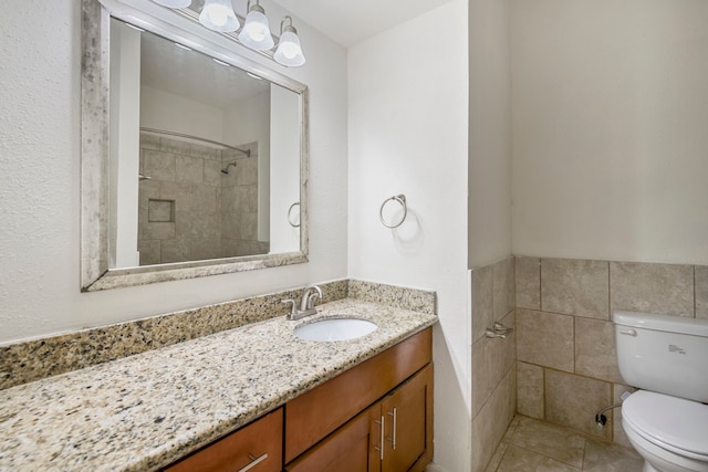 bathroom featuring vanity, tiled shower, tile patterned floors, tile walls, and toilet