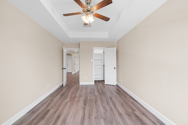 unfurnished bedroom with ceiling fan, a closet, a tray ceiling, a spacious closet, and light hardwood / wood-style floors