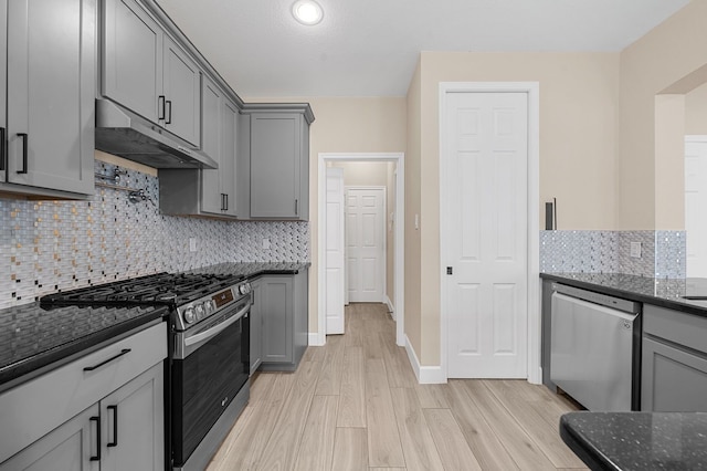 kitchen featuring appliances with stainless steel finishes, dark stone counters, light hardwood / wood-style floors, and gray cabinets