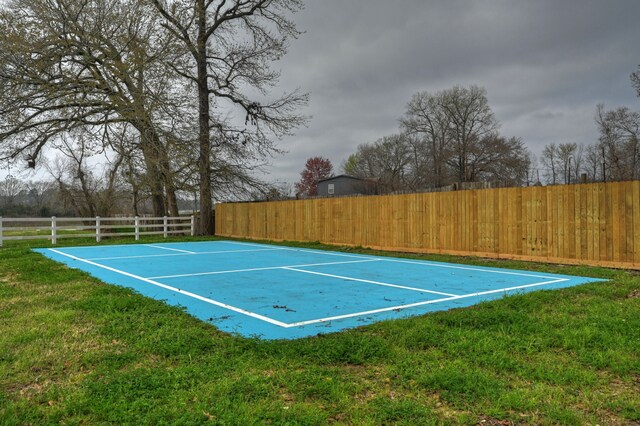 view of sport court featuring a lawn and basketball hoop