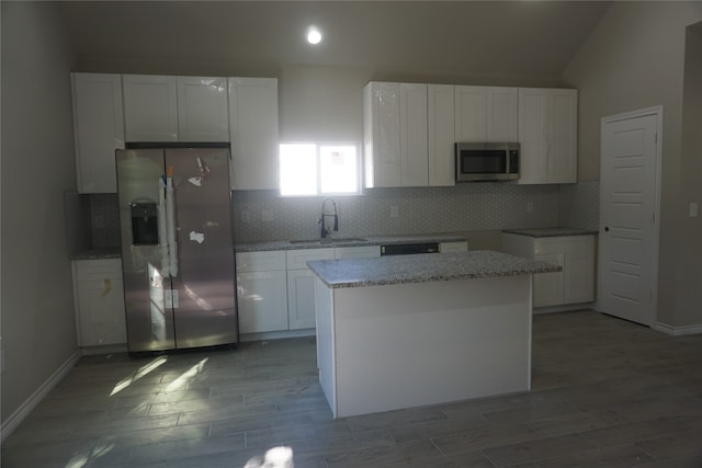 kitchen featuring a center island, vaulted ceiling, white cabinets, sink, and appliances with stainless steel finishes