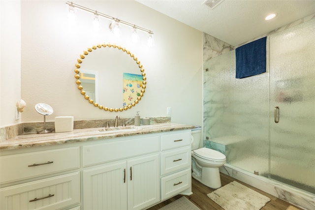 bathroom featuring a textured ceiling, hardwood / wood-style flooring, a shower with shower door, vanity, and toilet