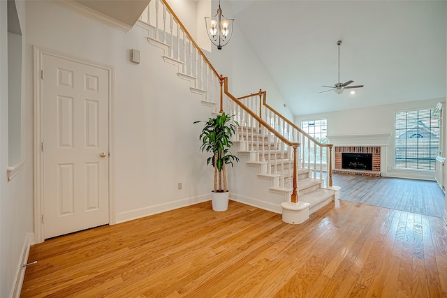 entrance foyer with ceiling fan with notable chandelier, high vaulted ceiling, light hardwood / wood-style flooring, and a fireplace