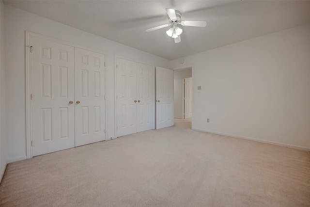 unfurnished bedroom with ceiling fan, light carpet, and multiple closets