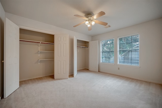 unfurnished bedroom with light carpet, multiple closets, and ceiling fan