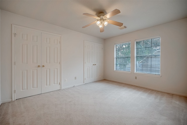 unfurnished bedroom featuring two closets, light colored carpet, and ceiling fan