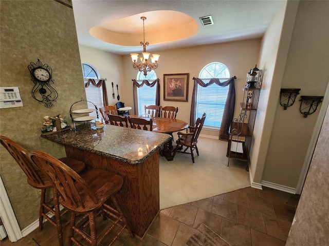 dining space featuring a notable chandelier, a raised ceiling, and dark colored carpet