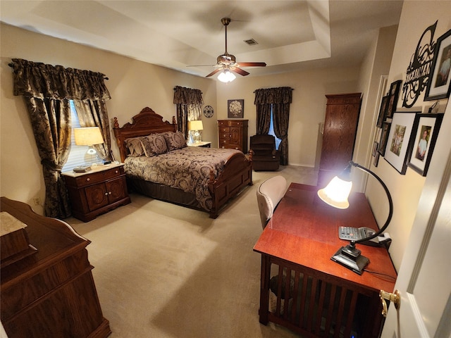 bedroom with ceiling fan, light colored carpet, and a tray ceiling