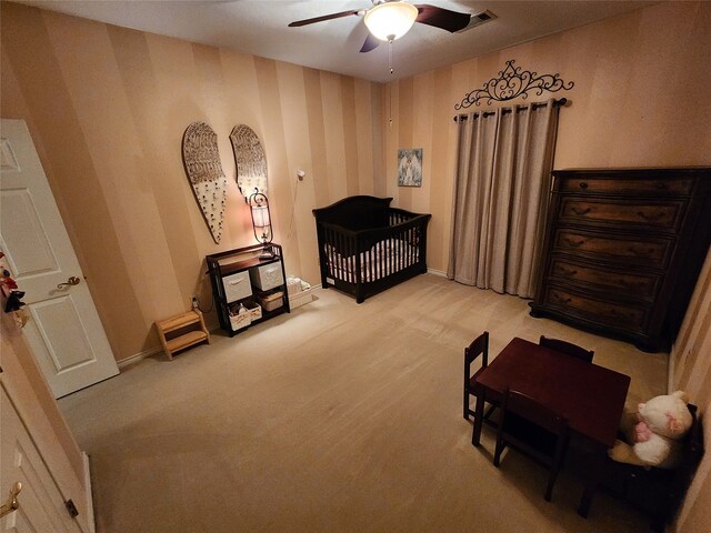 carpeted bedroom featuring ceiling fan and a nursery area