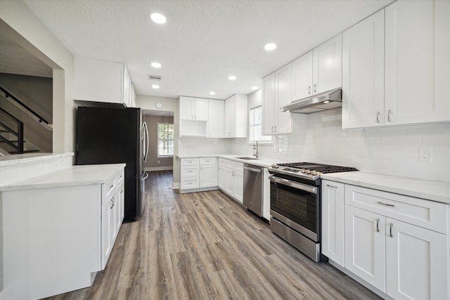 kitchen with appliances with stainless steel finishes, white cabinetry, a textured ceiling, light wood-type flooring, and light stone counters