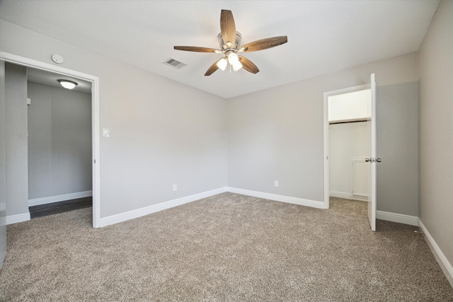 unfurnished bedroom with a walk in closet, carpet flooring, a closet, and ceiling fan