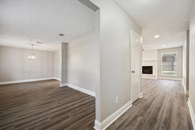 hallway featuring a textured ceiling, an inviting chandelier, and dark hardwood / wood-style flooring