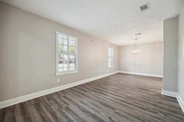 empty room with a textured ceiling, a notable chandelier, and dark hardwood / wood-style floors