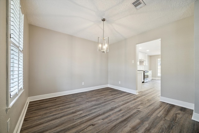 empty room with a textured ceiling, dark hardwood / wood-style floors, and an inviting chandelier