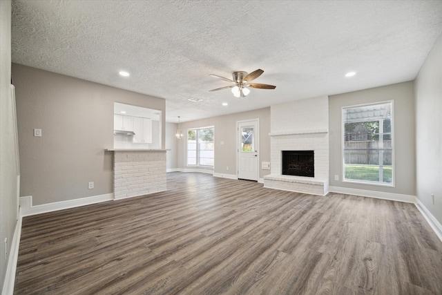 unfurnished living room featuring a textured ceiling, a brick fireplace, dark hardwood / wood-style floors, and ceiling fan