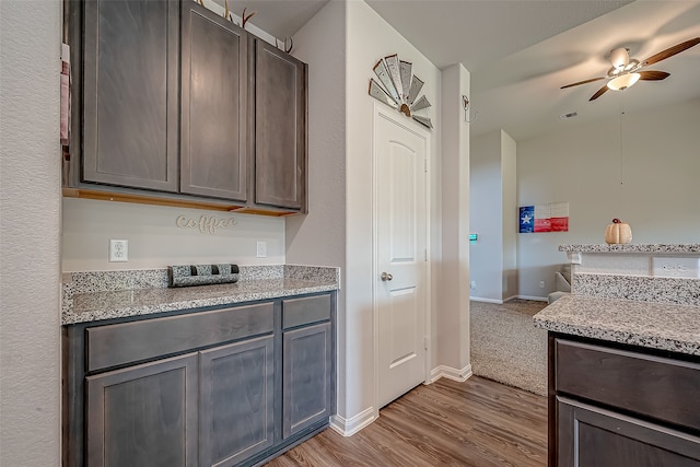 kitchen featuring ceiling fan, light stone countertops, dark brown cabinetry, and wood-type flooring