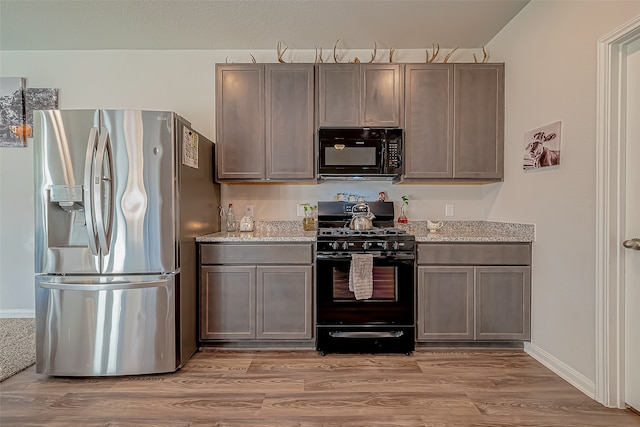 kitchen with black appliances, hardwood / wood-style flooring, light stone counters, and vaulted ceiling