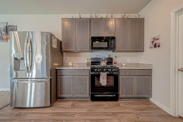 17624 Cedar Crest Dr, Conroe, TX 77306 - kitchen featuring black appliances, light wood finished floors, and light stone countertops
