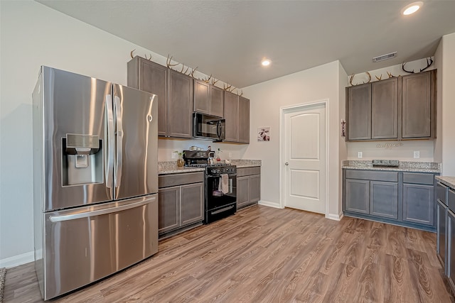 kitchen featuring light stone countertops, black appliances, and light hardwood / wood-style flooring