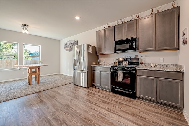 kitchen featuring dark brown cabinets, light stone counters, light hardwood / wood-style floors, and black appliances