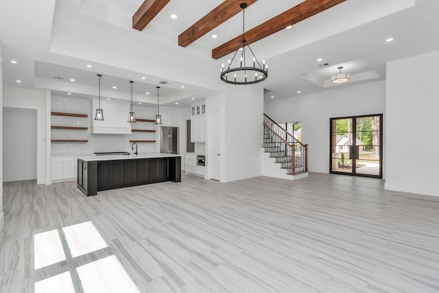 unfurnished living room with sink, beam ceiling, light hardwood / wood-style flooring, a chandelier, and a high ceiling