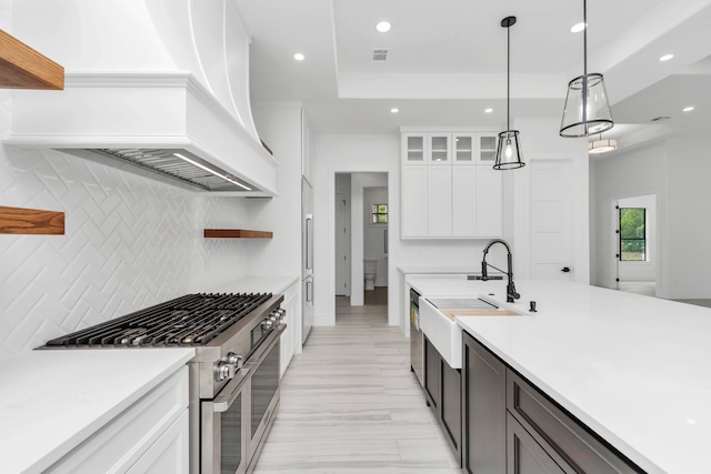 kitchen featuring white cabinetry, pendant lighting, high quality appliances, premium range hood, and sink