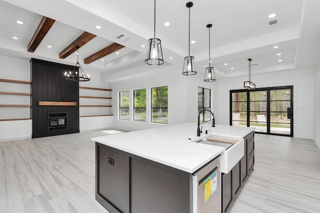 kitchen featuring pendant lighting, a large fireplace, an island with sink, and beamed ceiling