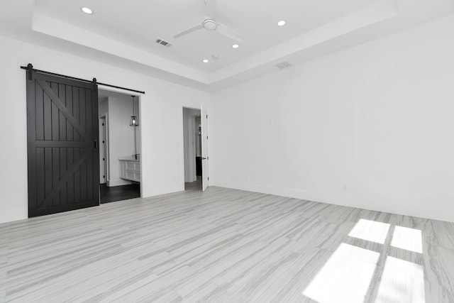 unfurnished room with a barn door, a raised ceiling, light wood-type flooring, and ceiling fan