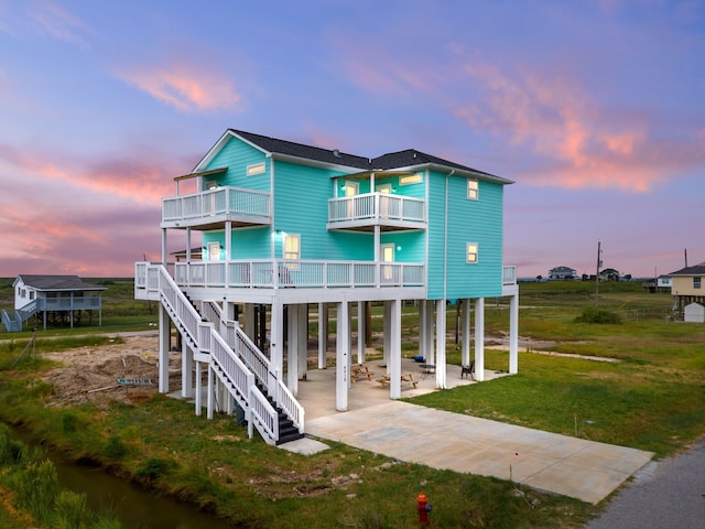 back house at dusk featuring a yard, a balcony, and a patio area