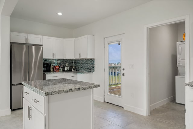 kitchen featuring light stone counters, stainless steel fridge, white cabinetry, a center island, and stacked washer / drying machine