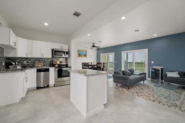 kitchen featuring appliances with stainless steel finishes, decorative backsplash, light stone counters, white cabinets, and a center island