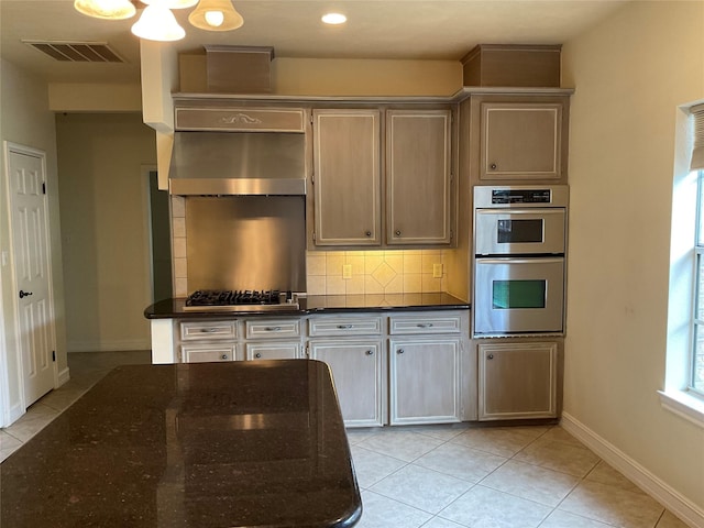 kitchen with wall chimney range hood, dark stone countertops, appliances with stainless steel finishes, tasteful backsplash, and light tile patterned flooring