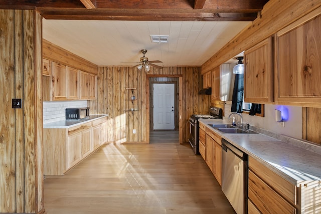 kitchen featuring ceiling fan, sink, wooden walls, stainless steel appliances, and light wood-type flooring