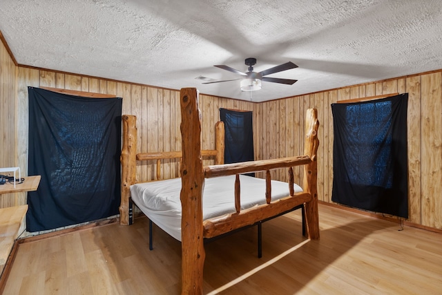 bedroom with a textured ceiling, wood walls, hardwood / wood-style floors, and ceiling fan