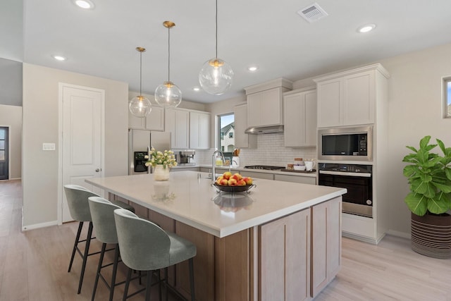 kitchen featuring under cabinet range hood, stainless steel appliances, visible vents, a large island, and decorative backsplash