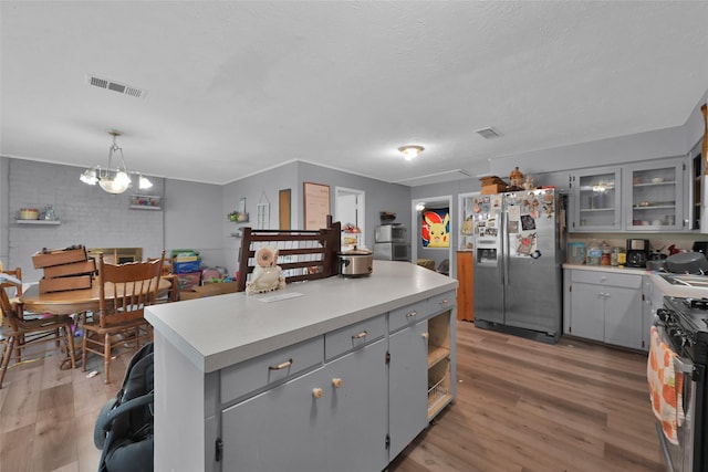 kitchen featuring a kitchen island, pendant lighting, gray cabinetry, gas stove, and stainless steel refrigerator with ice dispenser