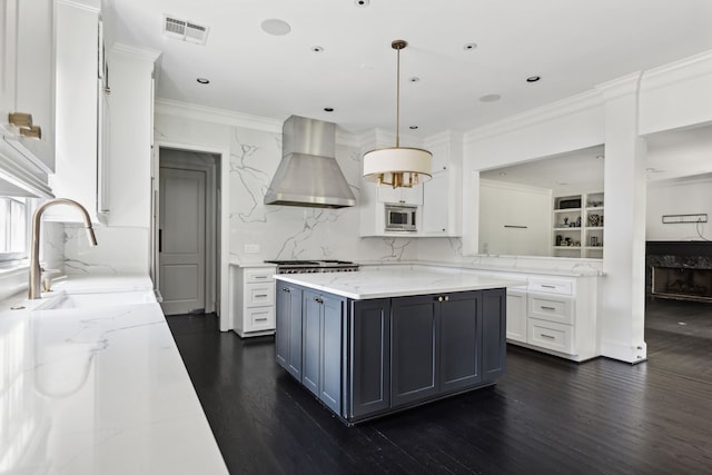 kitchen featuring sink, ventilation hood, stainless steel microwave, pendant lighting, and white cabinets