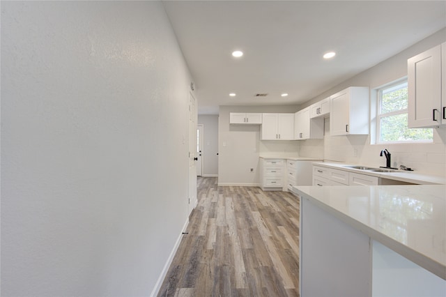 kitchen featuring white cabinets, light hardwood / wood-style flooring, backsplash, and sink