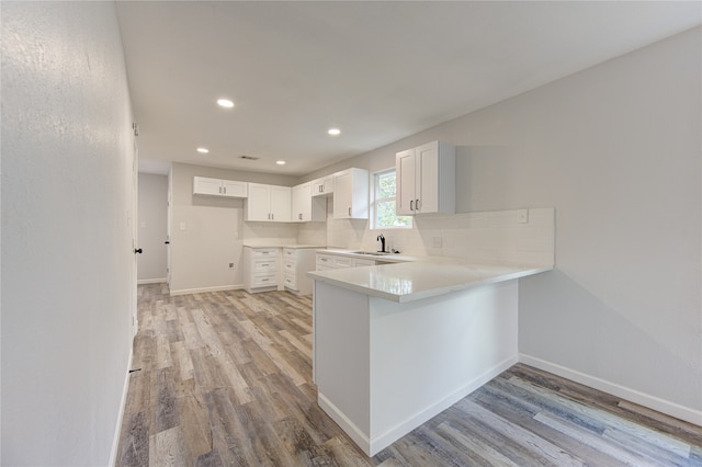 kitchen with tasteful backsplash, white cabinets, sink, kitchen peninsula, and light hardwood / wood-style flooring